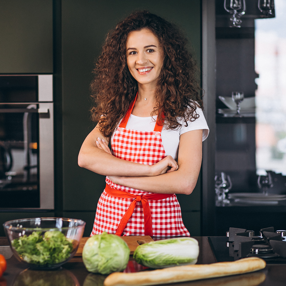 Woman in a kitchen wearing a red checkered apron with ingredients on the counter.
